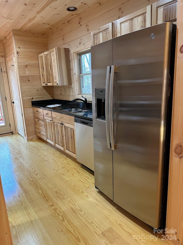 kitchen with appliances with stainless steel finishes, light brown cabinets, sink, light hardwood / wood-style flooring, and wood walls