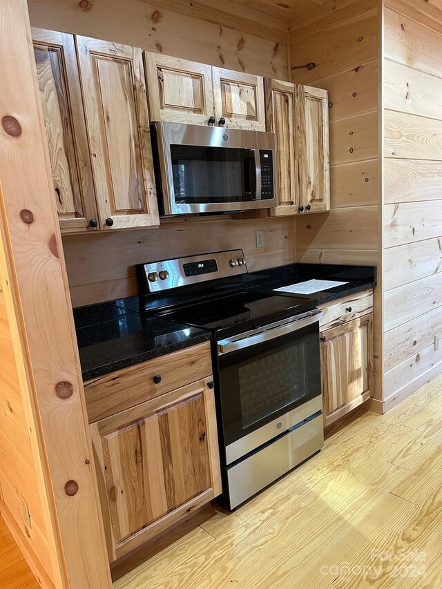 kitchen with wooden walls, stainless steel appliances, and light hardwood / wood-style floors