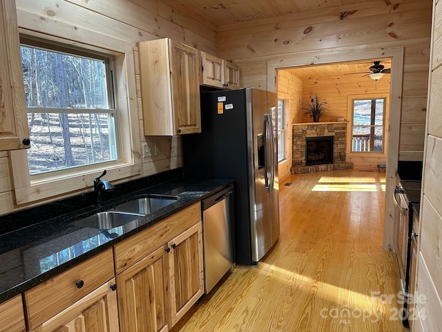 kitchen featuring stainless steel dishwasher, dark stone counters, wooden walls, light hardwood / wood-style flooring, and sink