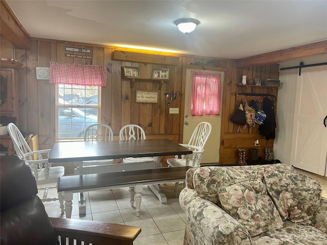 dining area featuring a barn door, wooden walls, and light tile flooring