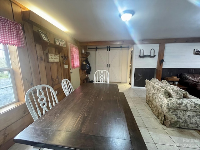 dining area featuring a barn door, wooden walls, and light tile flooring