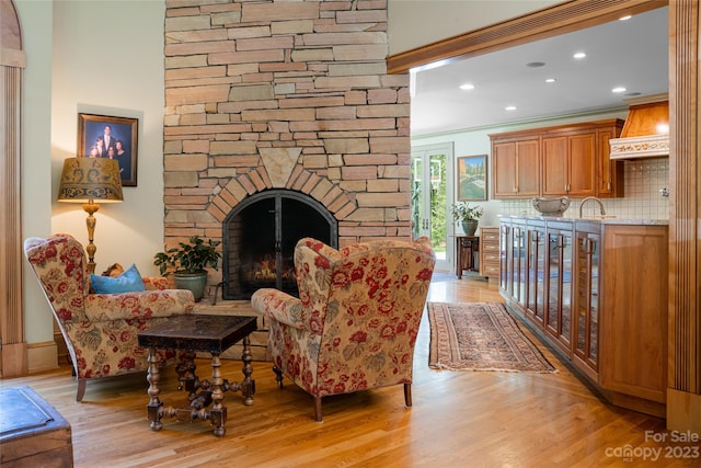 living room featuring crown molding, a fireplace, sink, and light wood-type flooring