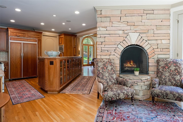 kitchen featuring built in appliances, ornamental molding, a fireplace, and light wood-type flooring