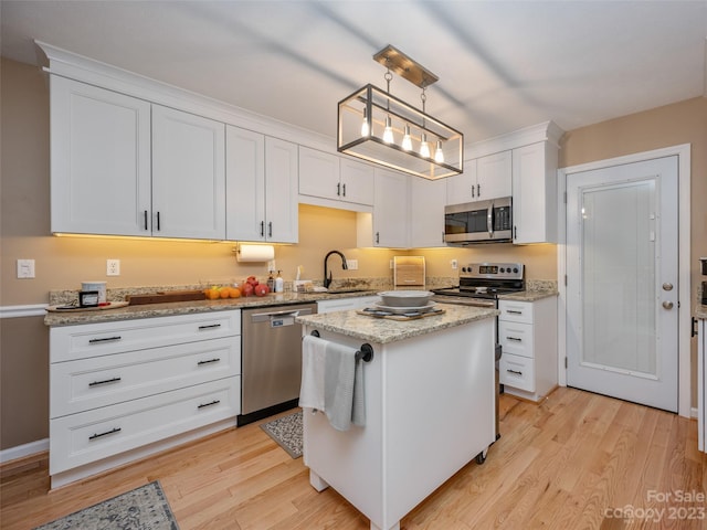 kitchen with appliances with stainless steel finishes, light wood-type flooring, a kitchen island, pendant lighting, and white cabinets