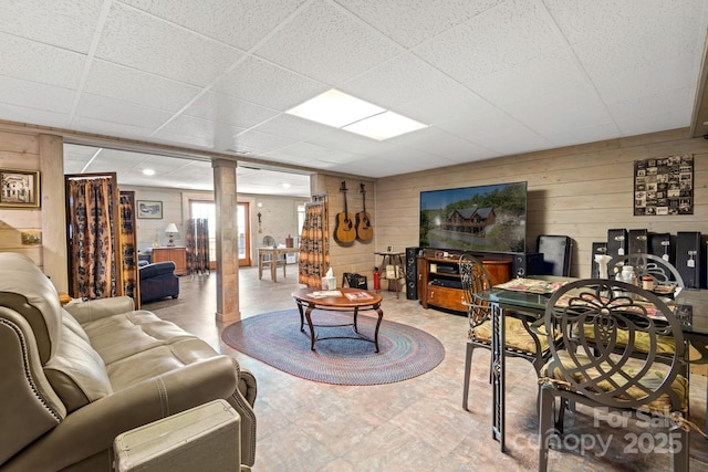 living room featuring decorative columns, a drop ceiling, and wooden walls