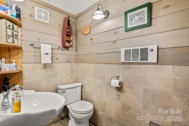 bathroom with toilet, sink, a textured ceiling, and wood walls