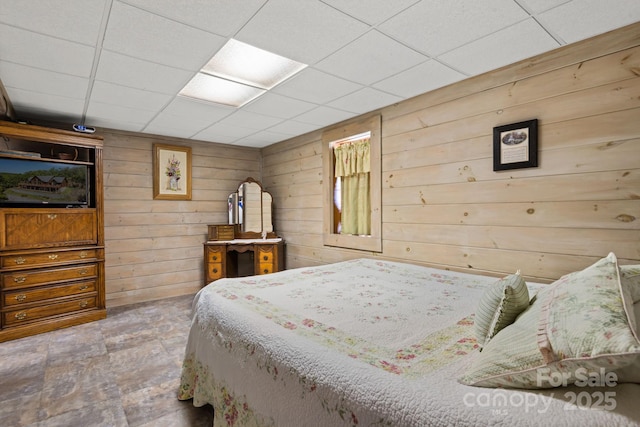 bedroom featuring a drop ceiling and wood walls