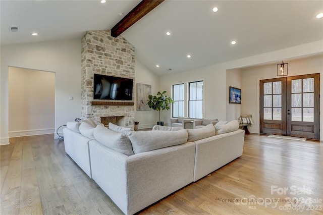 living room featuring light wood-type flooring, beamed ceiling, plenty of natural light, a stone fireplace, and french doors