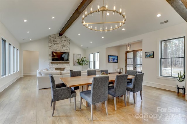 dining area featuring a stone fireplace, a chandelier, light wood-type flooring, and lofted ceiling with beams