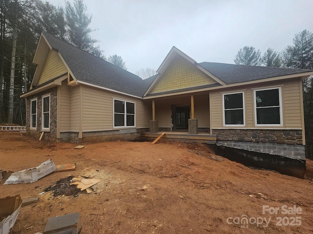 craftsman-style home featuring stone siding, covered porch, and roof with shingles