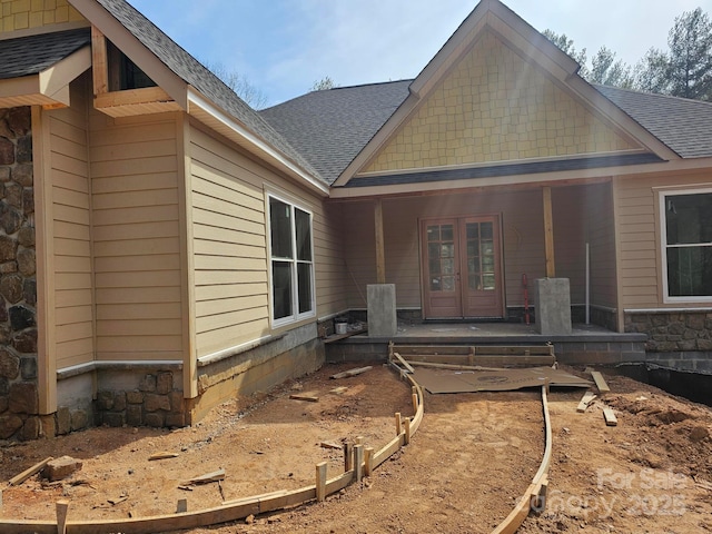 back of property featuring french doors, stone siding, and a shingled roof