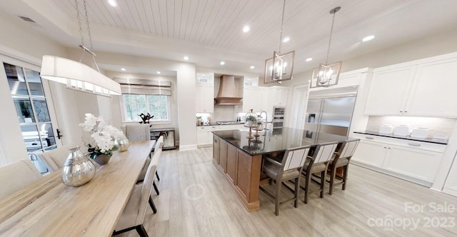 kitchen featuring hanging light fixtures, a kitchen island with sink, light hardwood / wood-style floors, white cabinets, and wall chimney exhaust hood