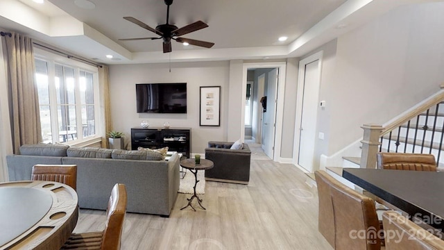 living room with ceiling fan, light hardwood / wood-style flooring, and a tray ceiling