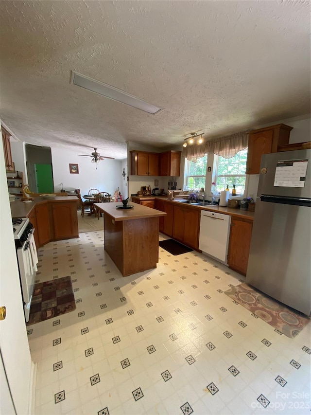 kitchen featuring light tile flooring, a kitchen island, ceiling fan, white appliances, and a textured ceiling