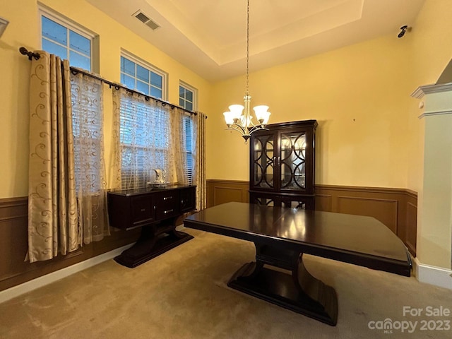 carpeted dining area with a notable chandelier and a raised ceiling