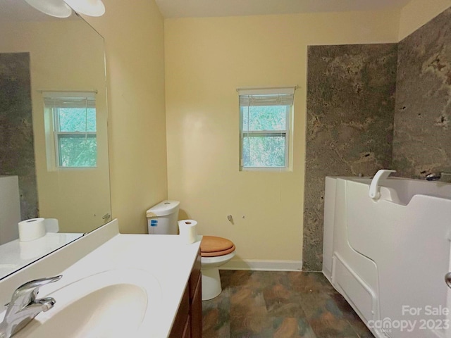 bathroom with large vanity, plenty of natural light, a washtub, and toilet