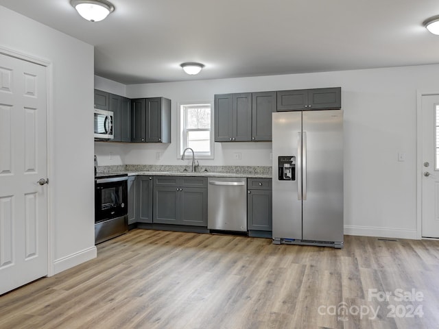 kitchen with gray cabinetry, sink, light stone countertops, appliances with stainless steel finishes, and light hardwood / wood-style floors