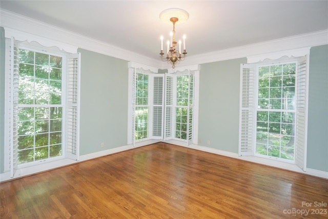 empty room featuring plenty of natural light, a notable chandelier, wood-type flooring, and crown molding