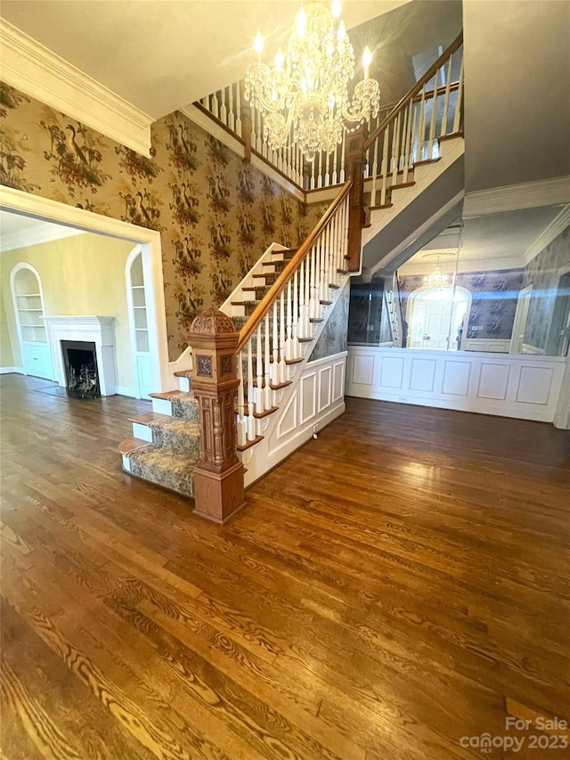 stairs featuring dark wood-type flooring, ornamental molding, and a chandelier