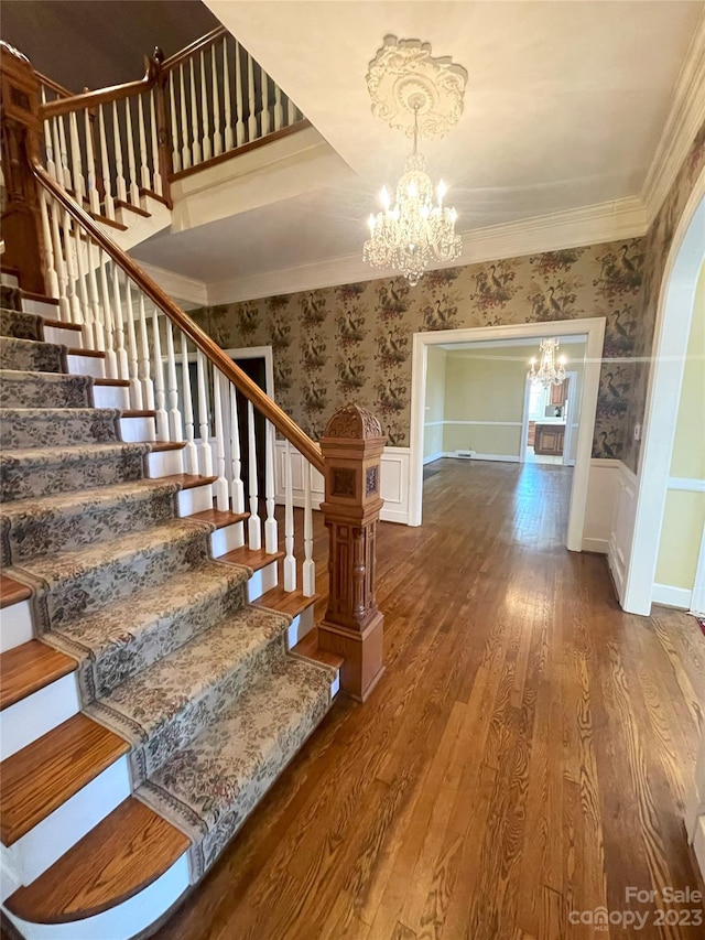 stairway with a chandelier, ornamental molding, and dark wood-type flooring