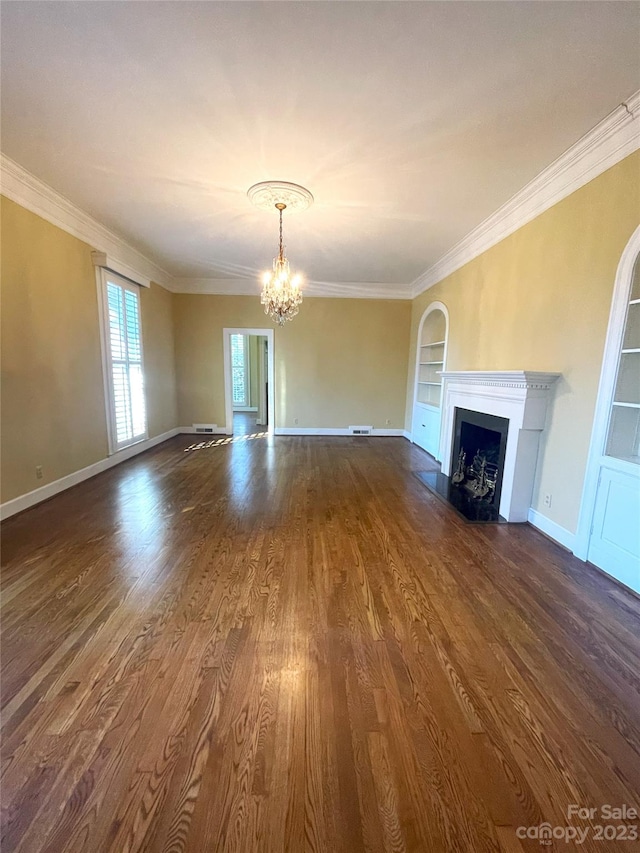 unfurnished living room with a chandelier, built in shelves, dark hardwood / wood-style floors, and crown molding