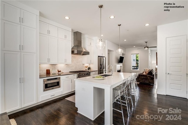 kitchen with a center island with sink, wall chimney exhaust hood, white cabinetry, and stainless steel appliances