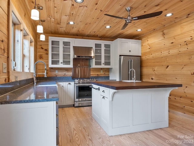 kitchen featuring ceiling fan, pendant lighting, light hardwood / wood-style floors, stainless steel appliances, and wall chimney exhaust hood