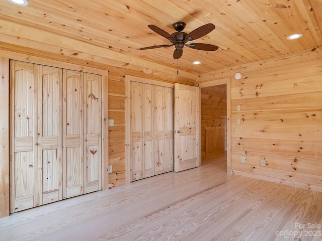 unfurnished bedroom featuring wooden walls, ceiling fan, light hardwood / wood-style flooring, wooden ceiling, and multiple closets