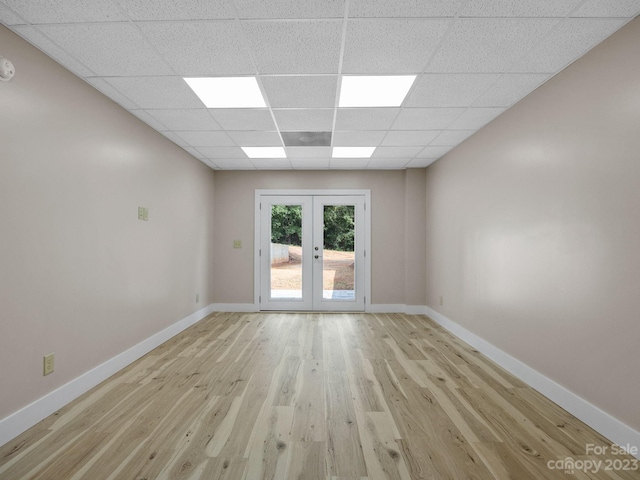 empty room featuring light wood-type flooring, a drop ceiling, and french doors