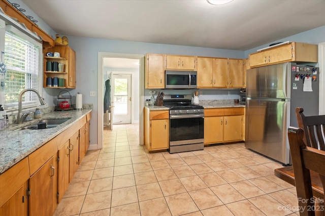 kitchen with appliances with stainless steel finishes, sink, light stone counters, and light tile floors