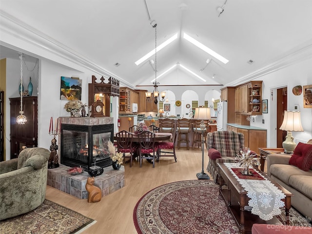 living room with a tile fireplace, light hardwood / wood-style floors, lofted ceiling with skylight, ornamental molding, and an inviting chandelier