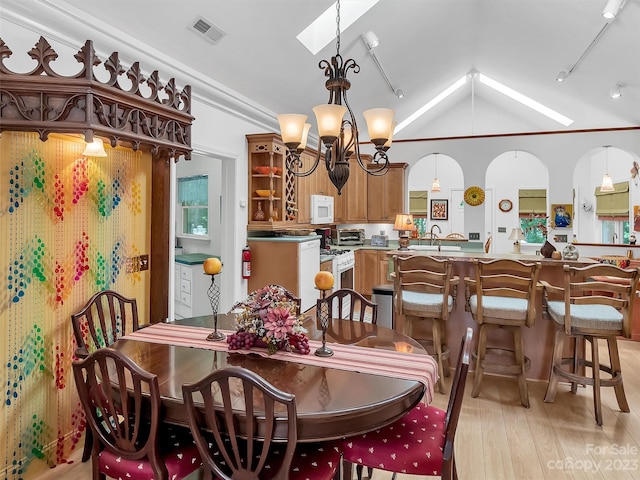 dining area with lofted ceiling with skylight, an inviting chandelier, light hardwood / wood-style flooring, track lighting, and sink