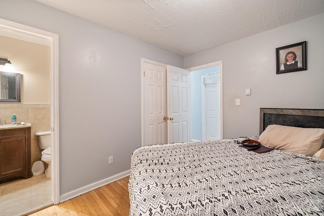 bedroom with tile walls, ensuite bathroom, light tile floors, and a textured ceiling