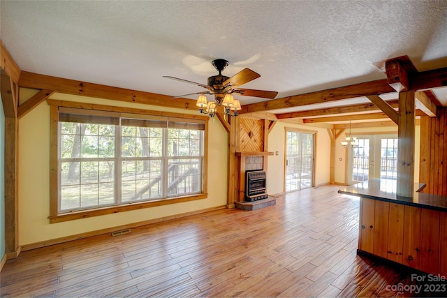 unfurnished living room featuring light hardwood / wood-style floors, beam ceiling, ceiling fan, a textured ceiling, and a wood stove