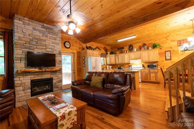 living room with wooden walls, ceiling fan with notable chandelier, light hardwood / wood-style floors, and a stone fireplace