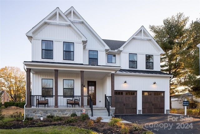 modern farmhouse featuring a standing seam roof, a porch, an attached garage, aphalt driveway, and board and batten siding