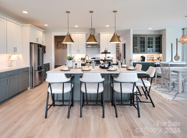 kitchen featuring high end fridge, pendant lighting, a center island with sink, gray cabinets, and white cabinetry