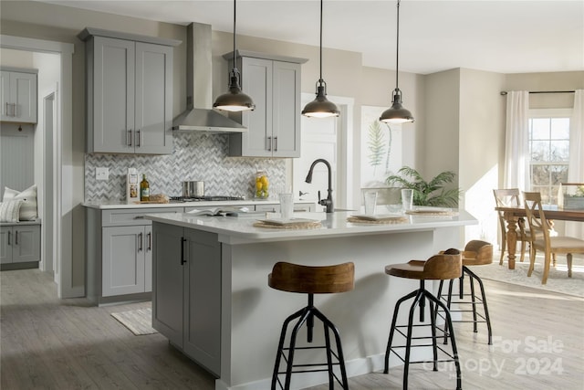 kitchen featuring decorative light fixtures, gray cabinets, a kitchen breakfast bar, and wall chimney range hood