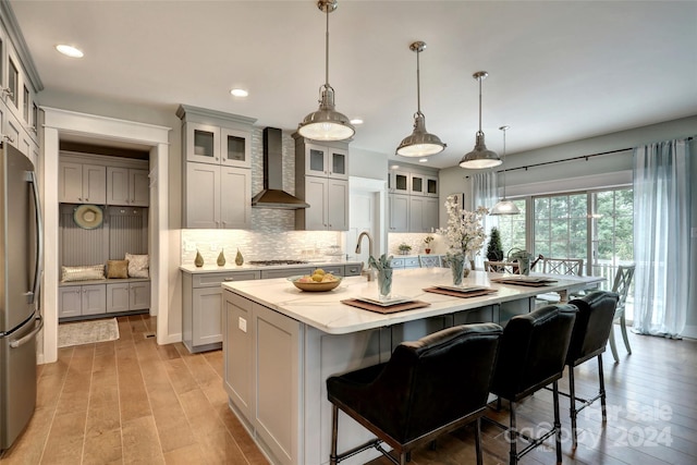 kitchen with stainless steel appliances, hanging light fixtures, wall chimney exhaust hood, and an island with sink