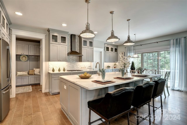 kitchen with backsplash, stainless steel appliances, light wood-style flooring, and wall chimney range hood