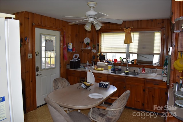 kitchen with wood walls, sink, ceiling fan, and white refrigerator