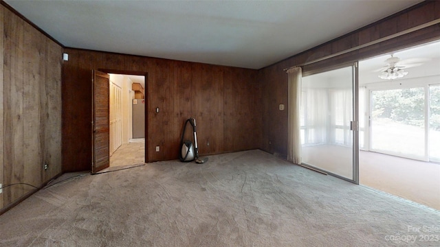 carpeted spare room with wooden walls and ceiling fan