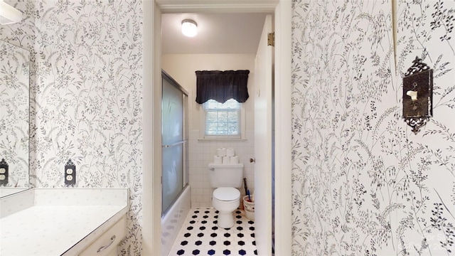 full bathroom with bath / shower combo with glass door, toilet, vanity, tile walls, and tile floors