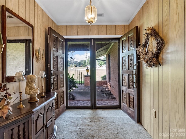 doorway with ornamental molding, light colored carpet, wood walls, and a chandelier