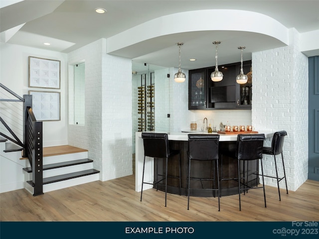 bar with light hardwood / wood-style flooring, tasteful backsplash, decorative light fixtures, and sink