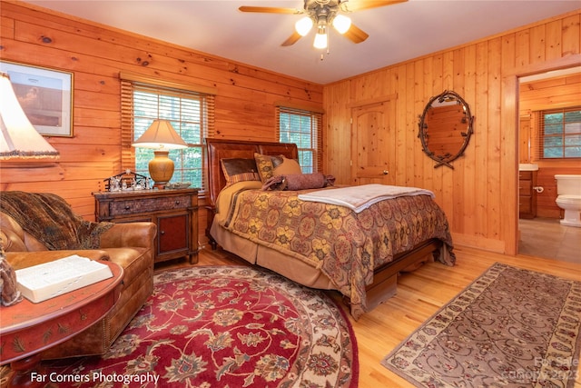 bedroom featuring wood walls, connected bathroom, light hardwood / wood-style floors, and ceiling fan