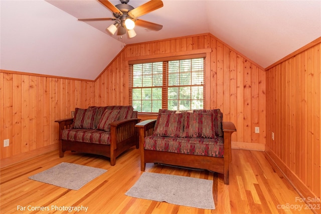 living area featuring wood walls, ceiling fan, vaulted ceiling, and light hardwood / wood-style flooring