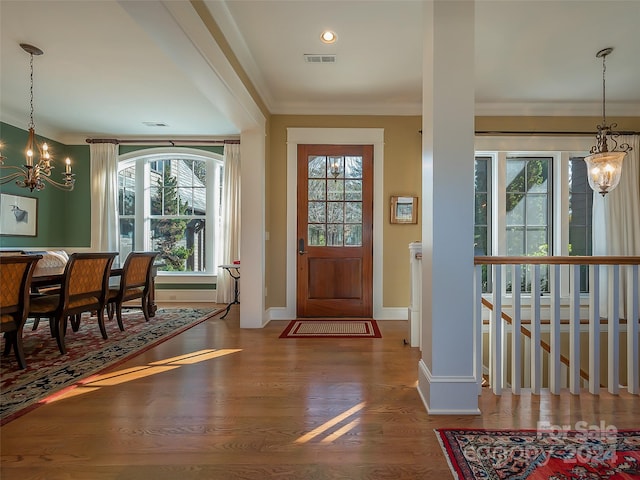 entrance foyer with a notable chandelier, ornamental molding, dark wood-type flooring, and a wealth of natural light