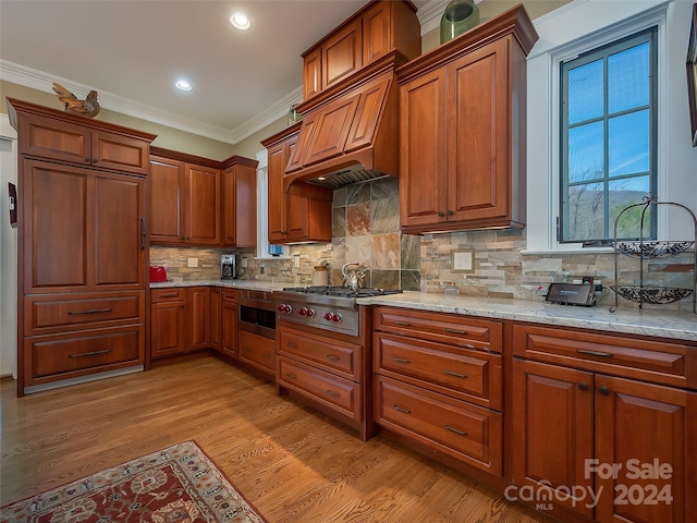 kitchen featuring light stone counters, ornamental molding, light hardwood / wood-style flooring, custom range hood, and tasteful backsplash