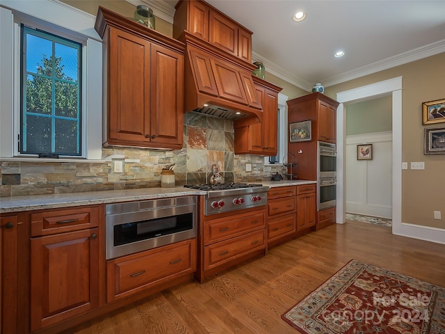 kitchen featuring light stone counters, appliances with stainless steel finishes, light hardwood / wood-style floors, premium range hood, and tasteful backsplash